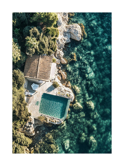 Overhead shot of a villa with pool next to turquoise water and rocky shore. Ideal for wall art in your home, office, or studio.