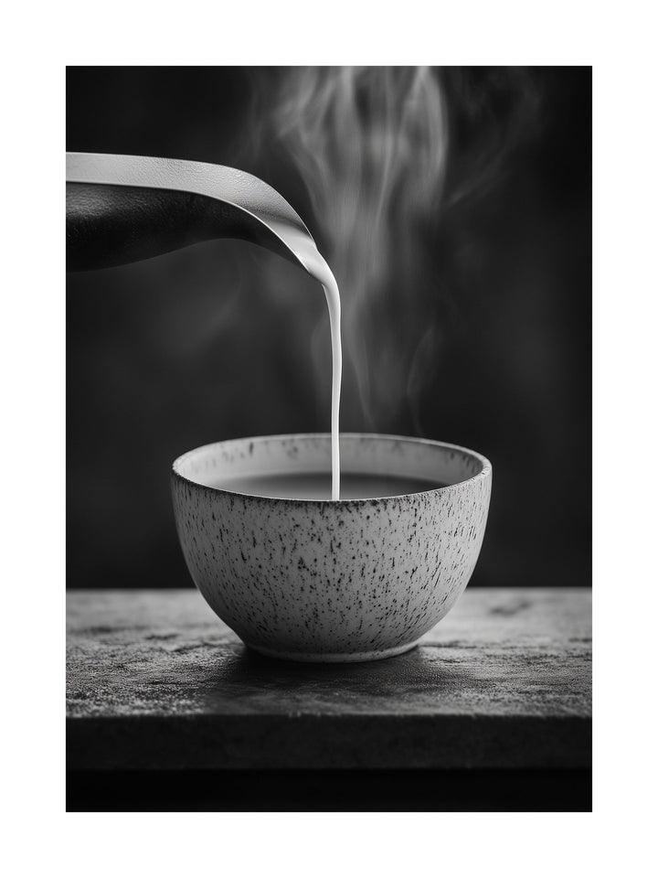 Steam rises as milk pours into a ceramic bowl in black and white