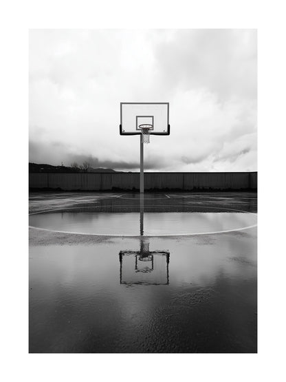 Black and white photo of basketball hoop and reflection on wet court