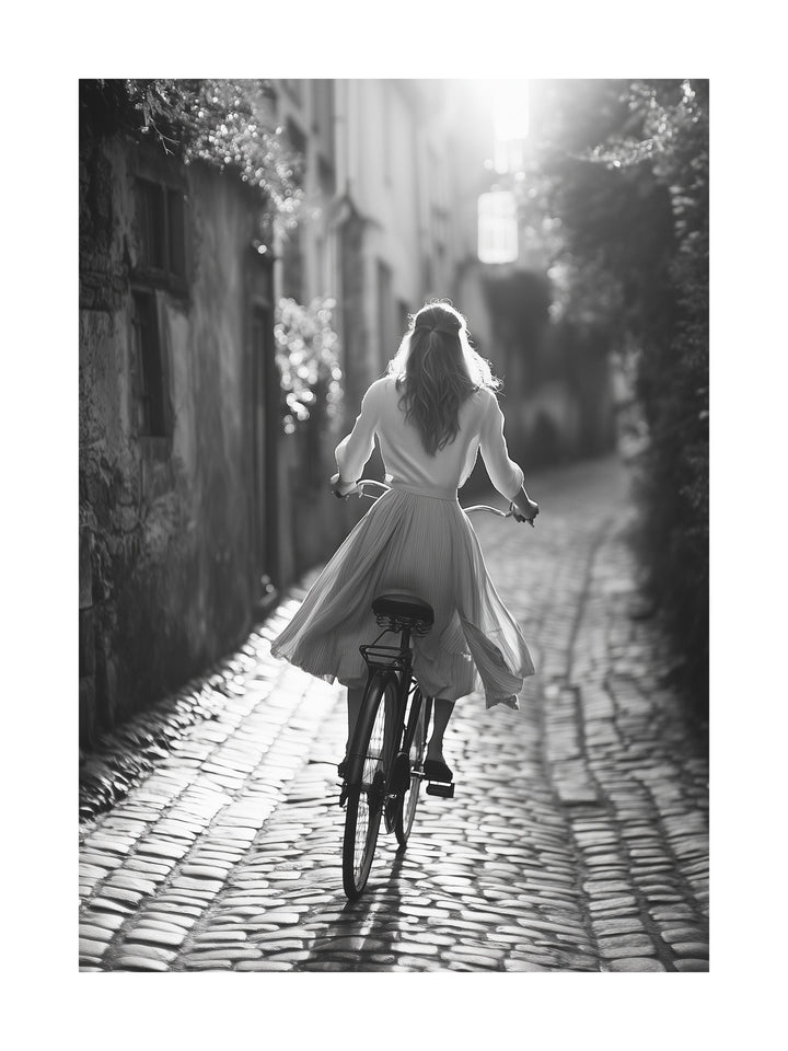 Black and white photo of a woman riding a bicycle on cobblestone street
