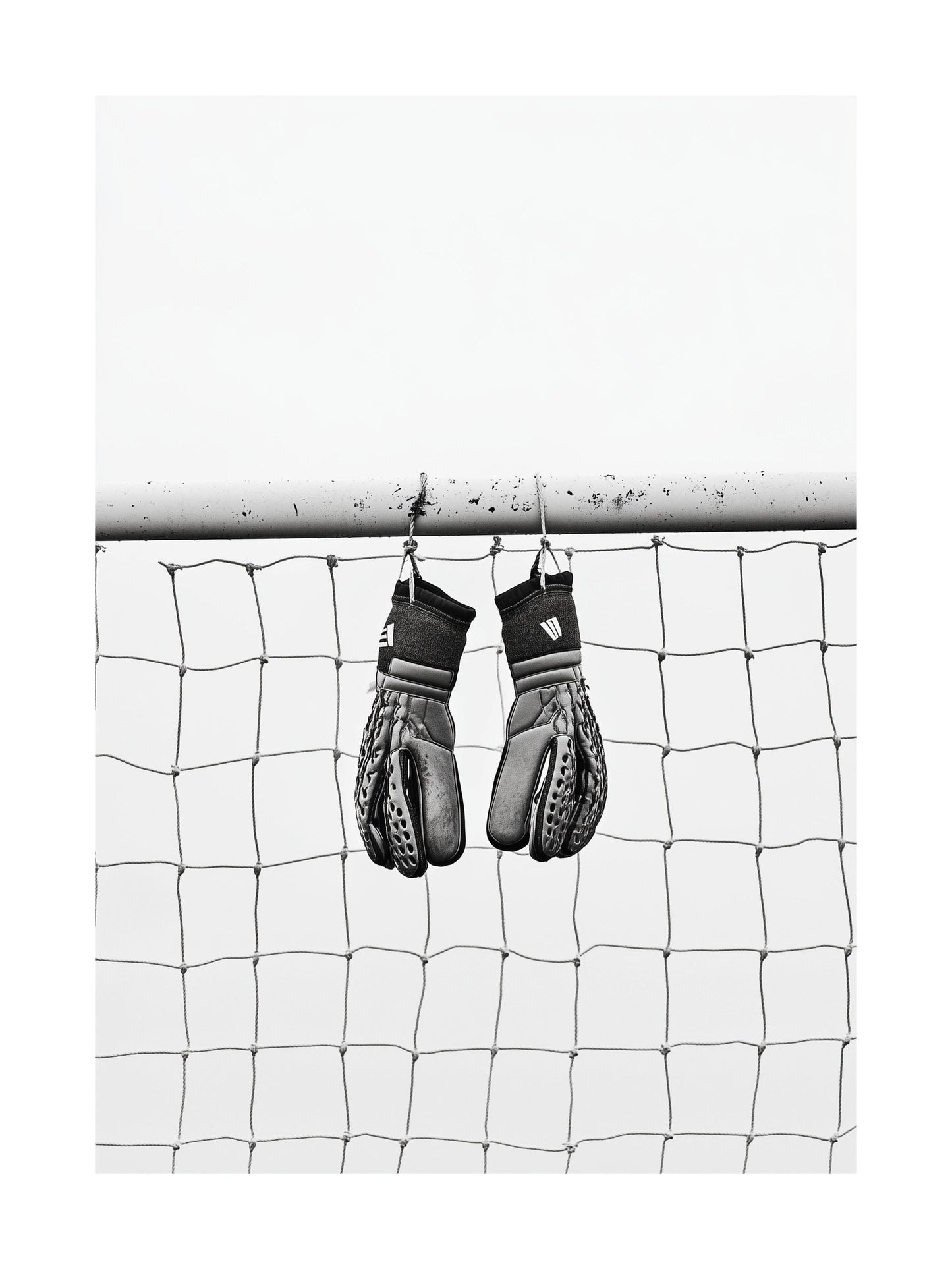 Black and white image of goalkeeper gloves hanging on goalpost