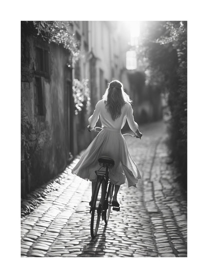 Black and white photo of a woman riding a bicycle on cobblestone street