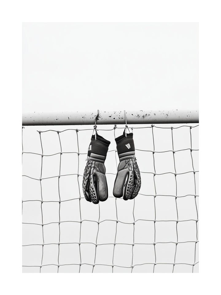 Black and white image of goalkeeper gloves hanging on goalpost