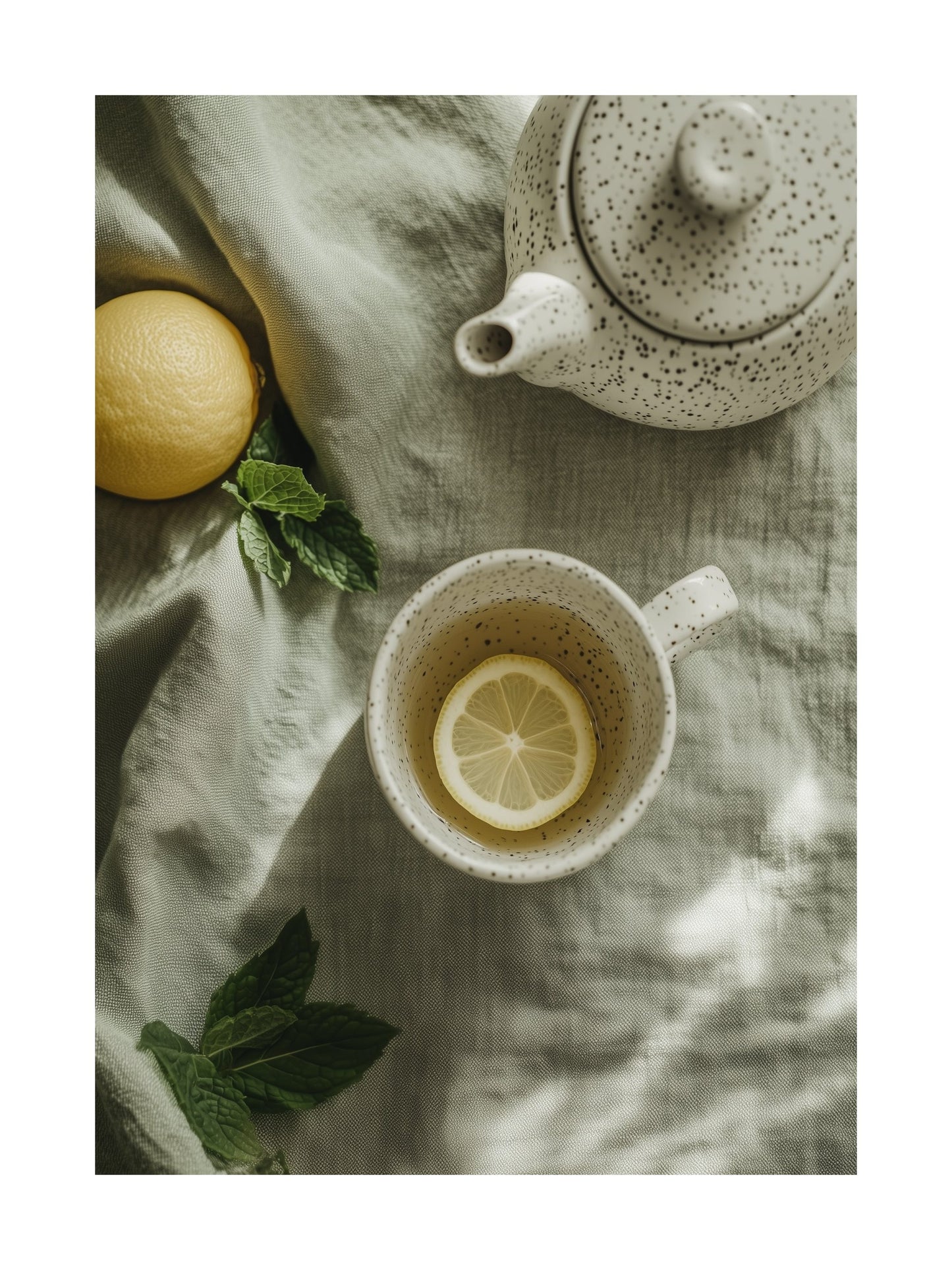 Flat lay of teacup with lemon slice and teapot on soft green fabric
