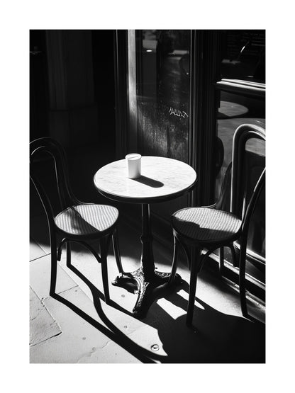Black and white photo of a sunlit café table with two chairs